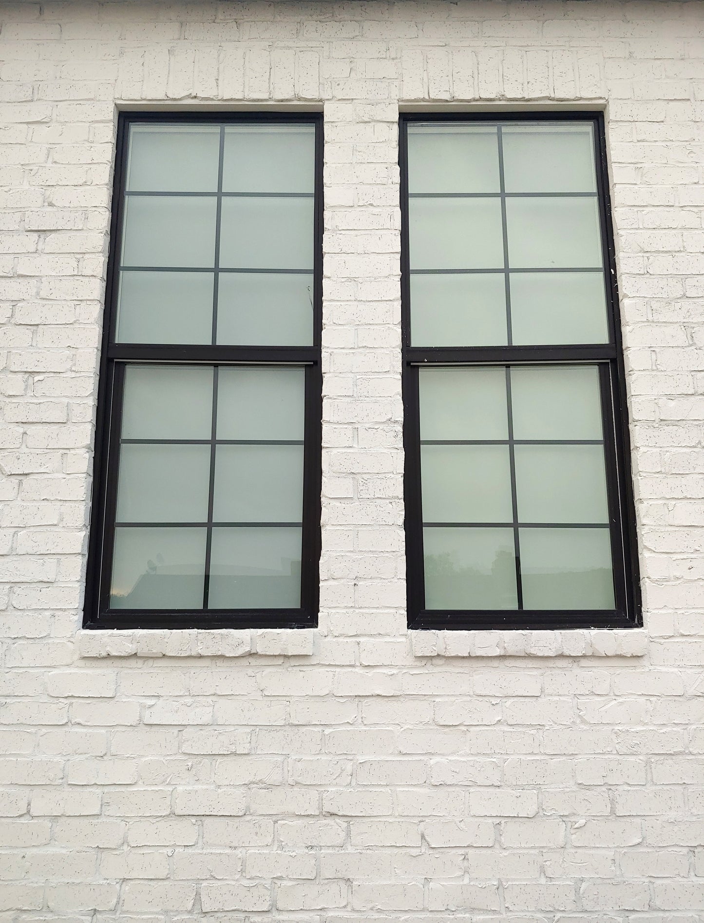 Exterior view of two black-trimmed vertical windows on white painted brick wall from FARMHOUSE Plan No.6 by Authentic Homes Builder in Utah.
