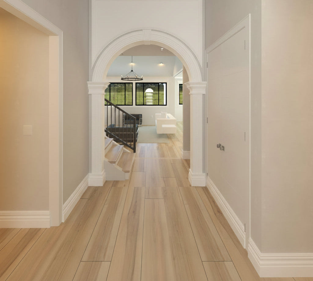 A modern interior hallway with light wood flooring, white walls, and an arched opening looking into a bright room with a staircase and windows.