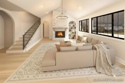 A modern open living space with light wood flooring, a white sectional sofa in the foreground, two gray sofas, a stone fireplace, a staircase on the left, and large black-framed windows looking out to water.