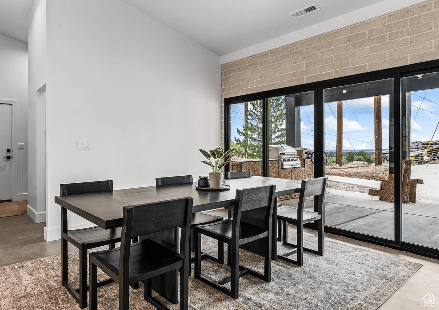 Modern dining area in Authentic Homes builder's Utah house plan featuring black dining set, large sliding glass doors, and exposed Omniblock wall. Bult in Provo, Utah by Authentic Homes.